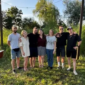 Grupa ośmiu osób pozujących do zdjęcia na tle zielonych roślin i drzew.